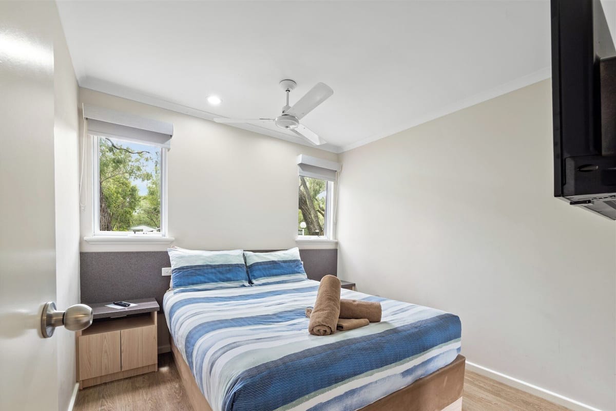 A bedroom with a bed, nightstands, a ceiling fan, and two windows.