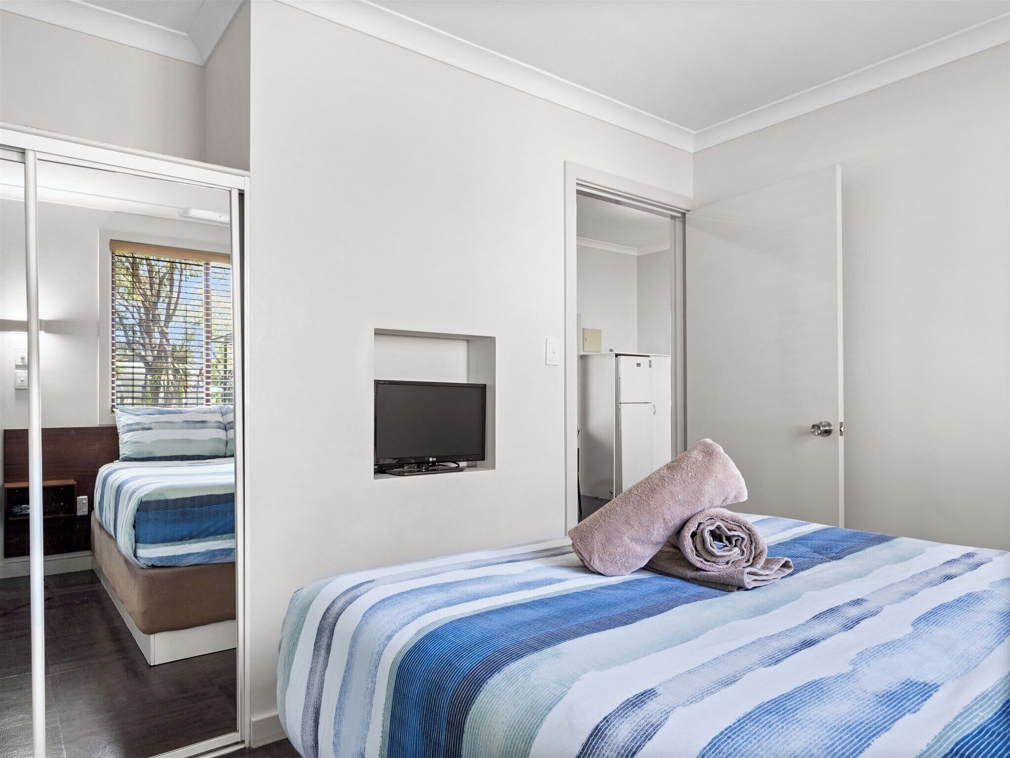 A bedroom with a bed, a television mounted on the wall, and a door leading to another room.