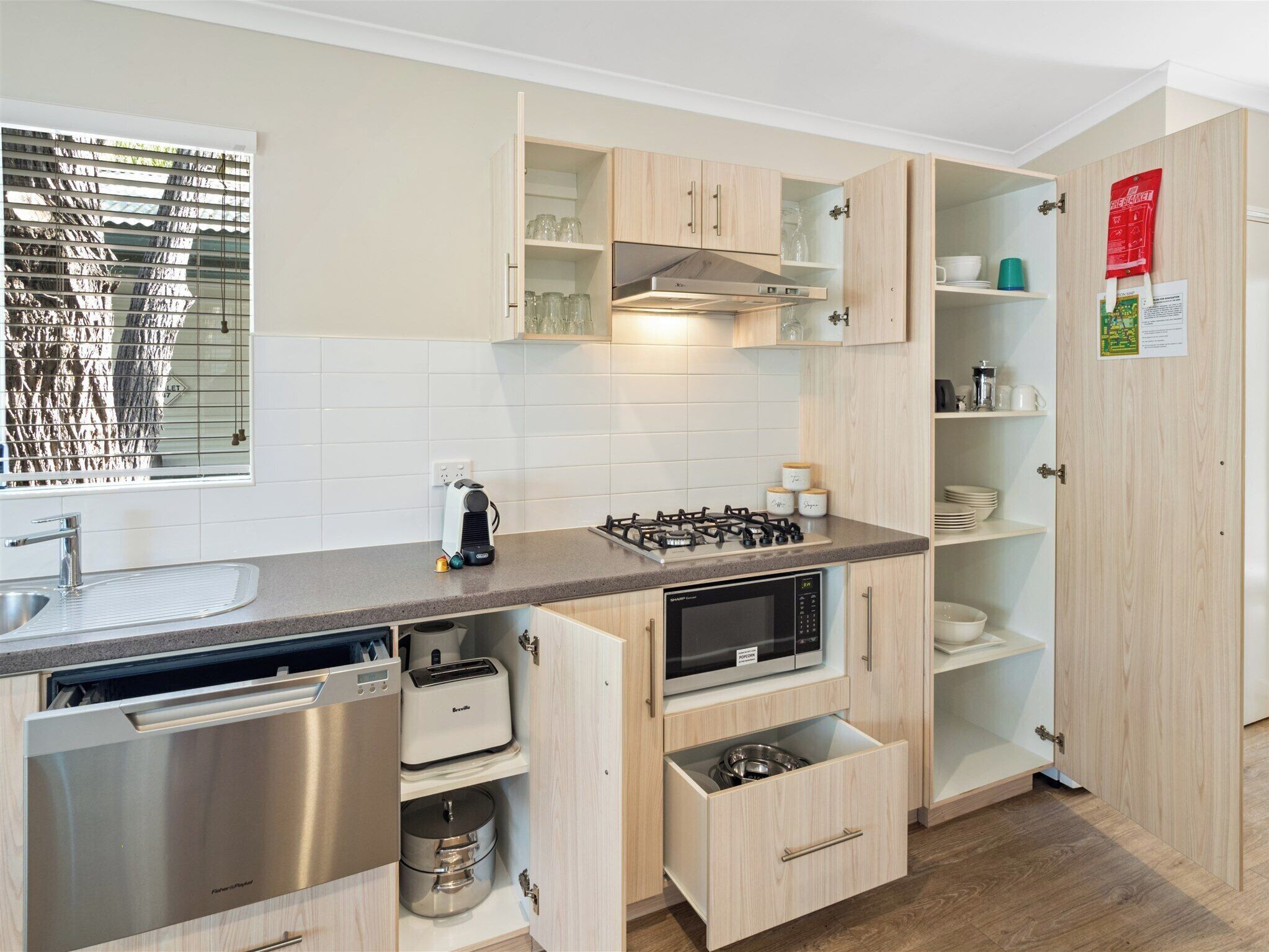 Una cocina moderna con electrodomésticos integrados, armarios de madera y un ventanal con persianas.