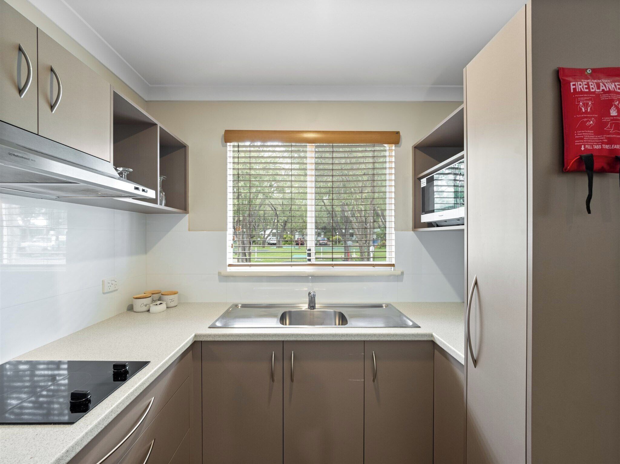 A modern kitchen with a stainless steel sink, a built-in oven, and a window with blinds.