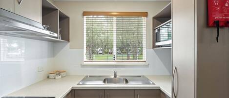 Una cocina moderna con un lavamanos de acero inoxidable, horno empotrado y ventana con persianas.
