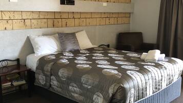 A hotel room with a brick-patterned headboard, a bed with a patterned duvet, a bedside table with books, and a dark-colored armchair.