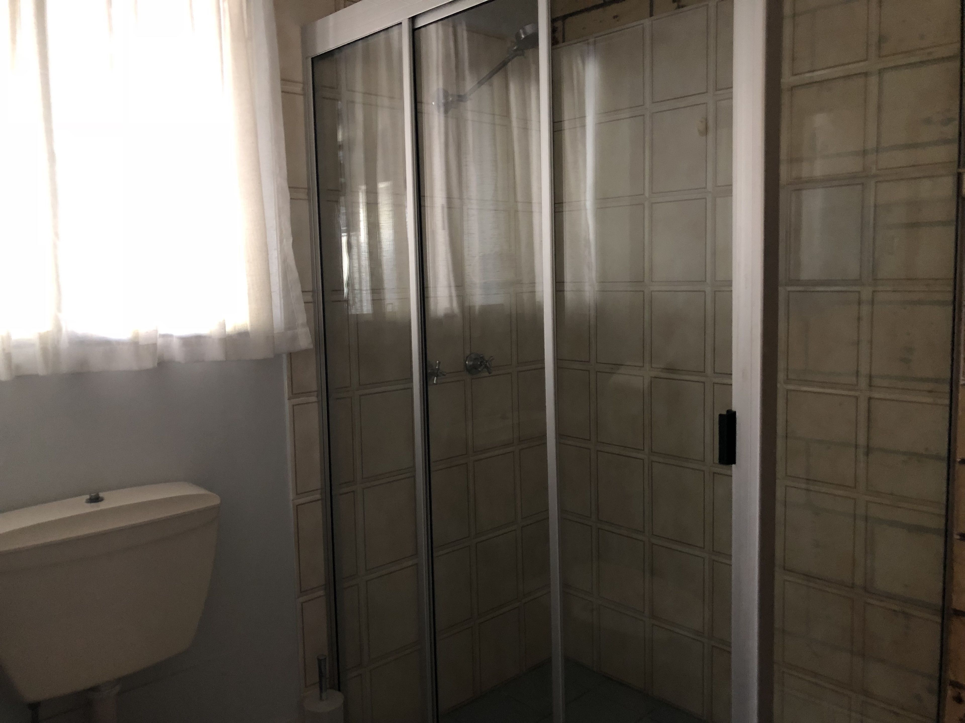 Een badkamer met toilet, een douchecabine van glas en betegelde wanden.