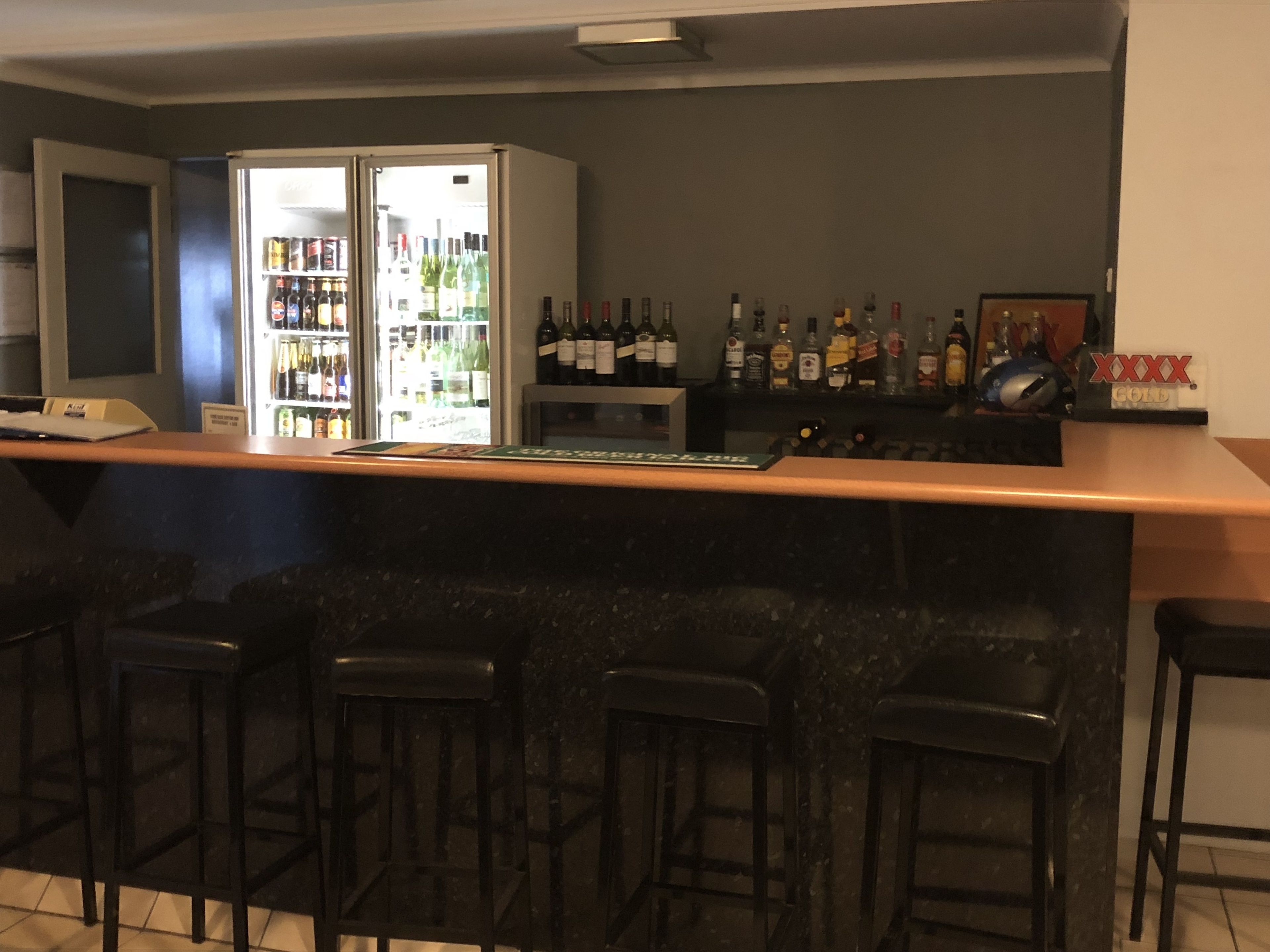 A bar area with a refrigerator stocked with beverages, a bar counter, and several stools.