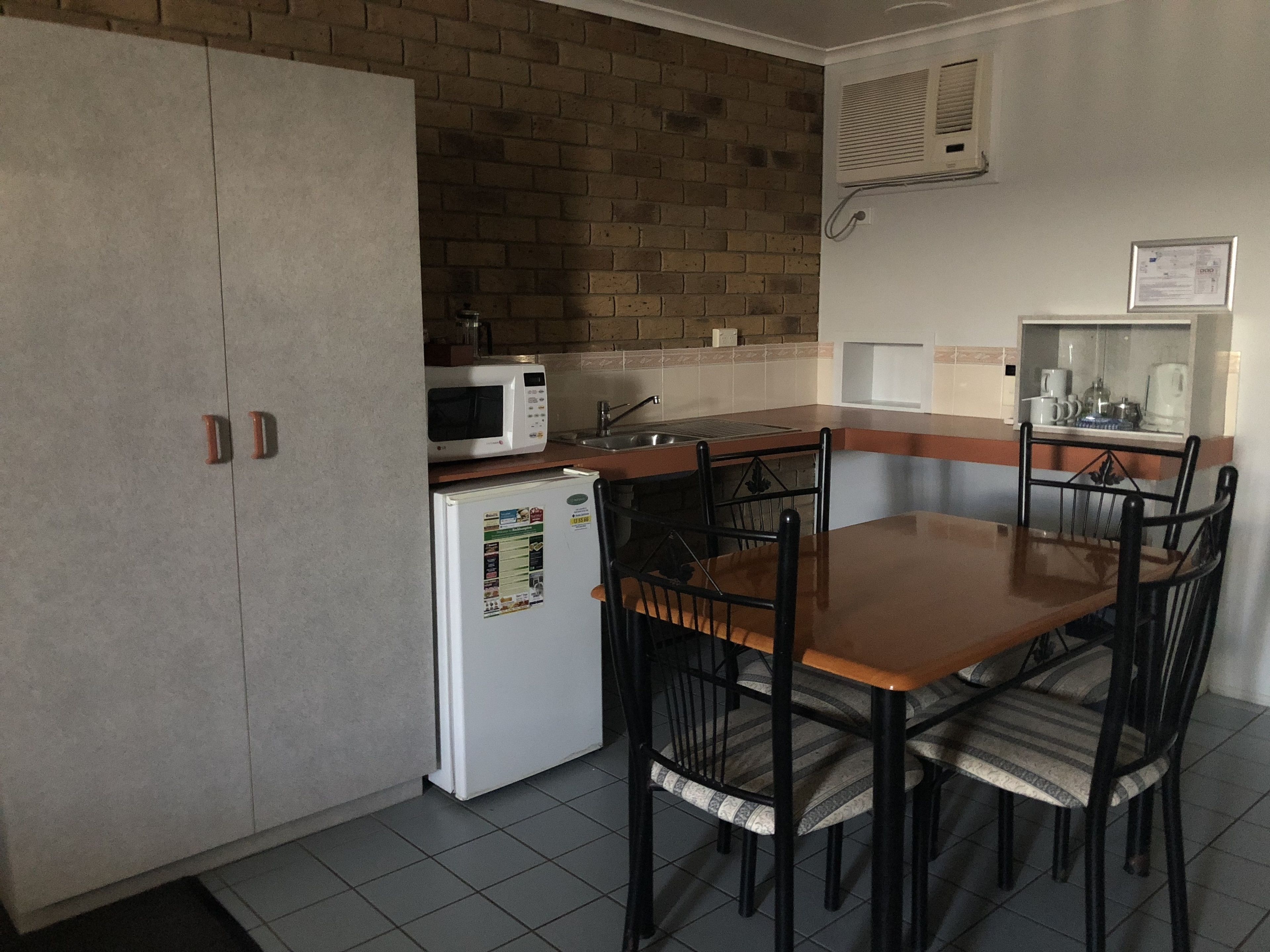 A compact kitchen with a microwave, refrigerator, and sink. There is a dining table with four chairs.