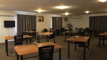 A conference room with multiple tables and chairs, a flat-screen TV mounted on the wall, and a small plant on one table.