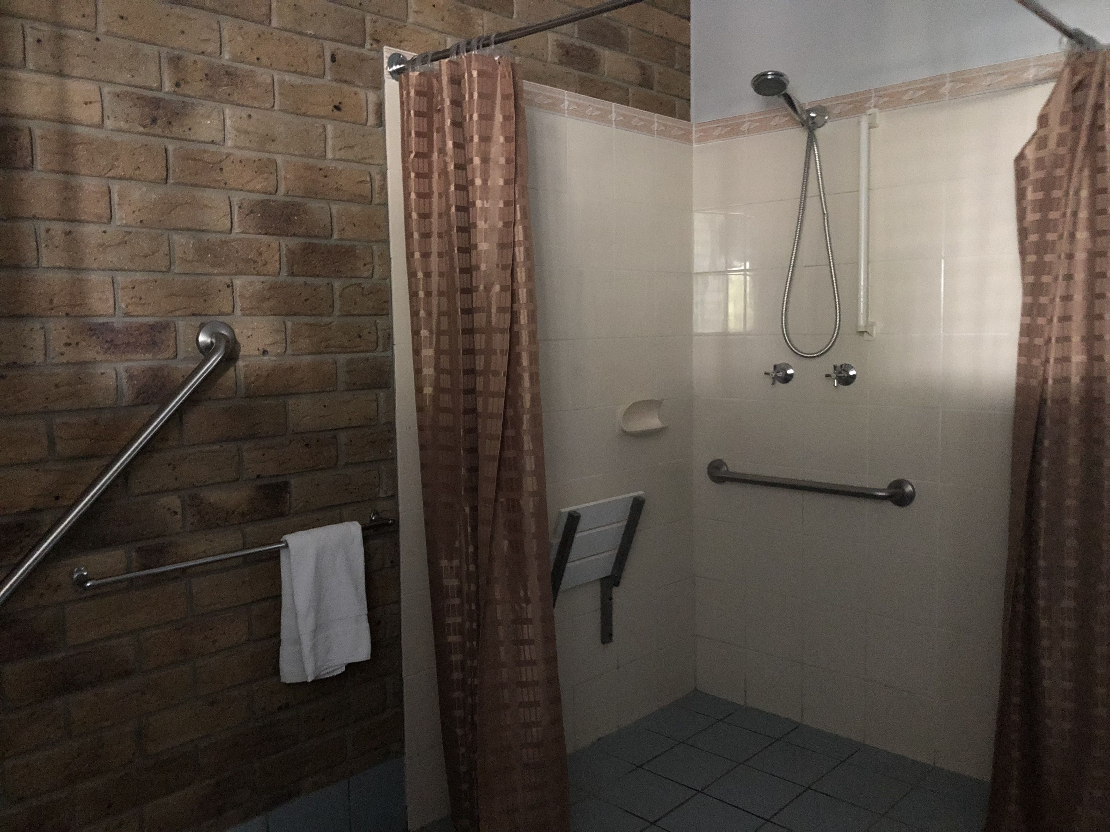 A shower area with a brick wall, a metal grab bar, a white towel, and a showerhead.