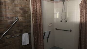 A shower area with a brick wall, a metal grab bar, a white towel, and a showerhead.