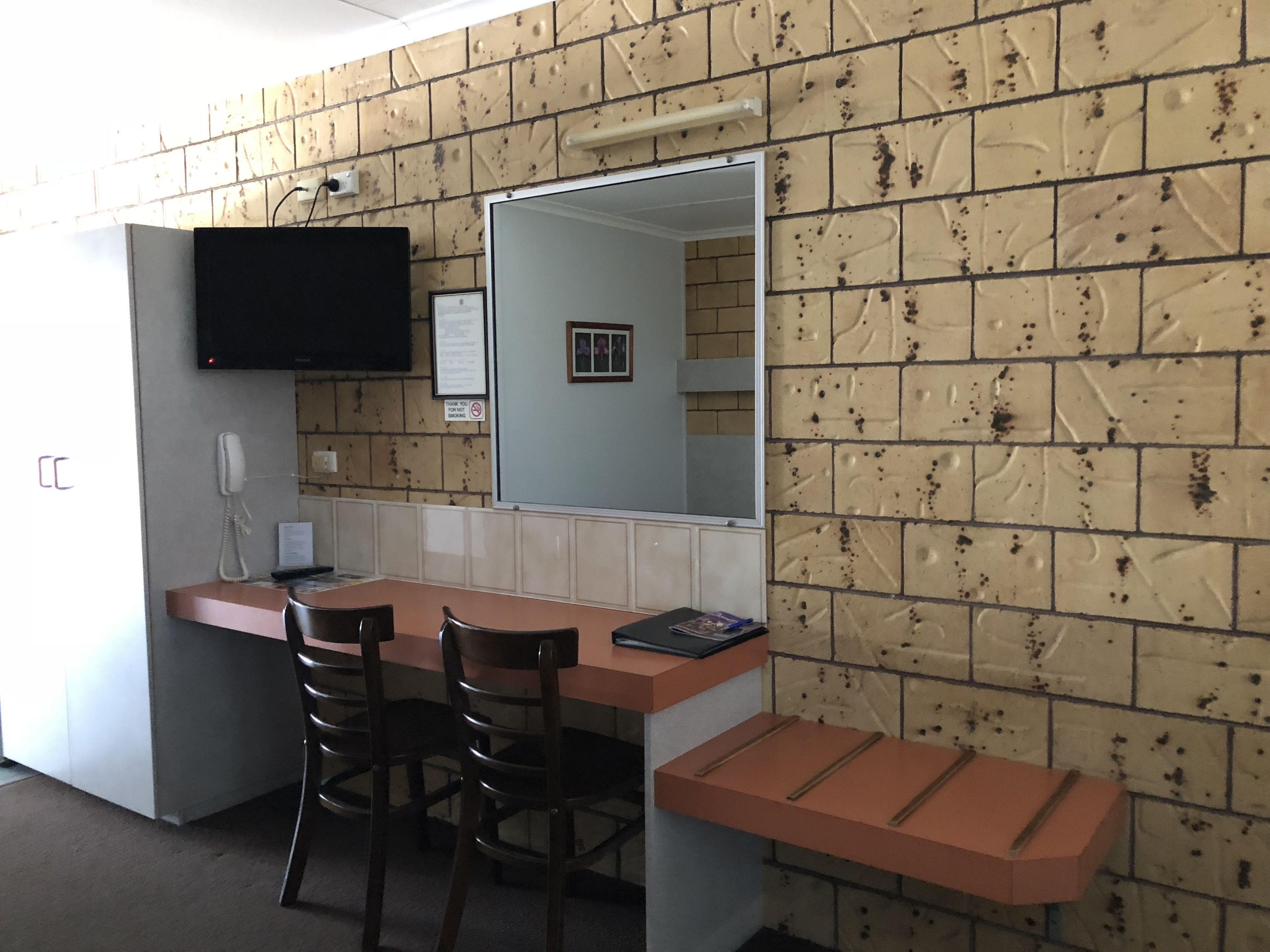 A small, compact room with a kitchenette, a mirror, and a television mounted on the wall.
