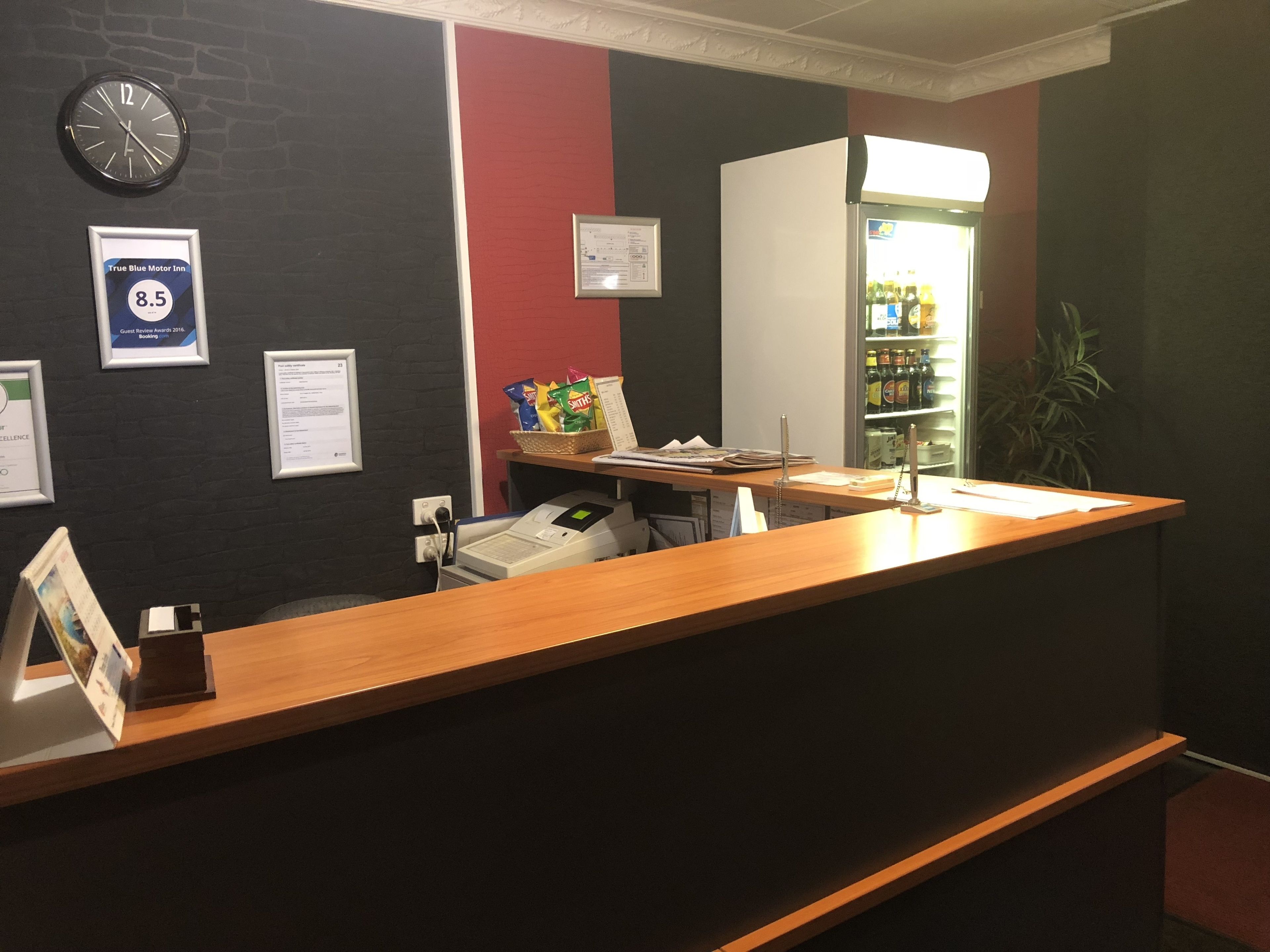 A reception desk with a clock, framed awards, and a refrigerator stocked with beverages.