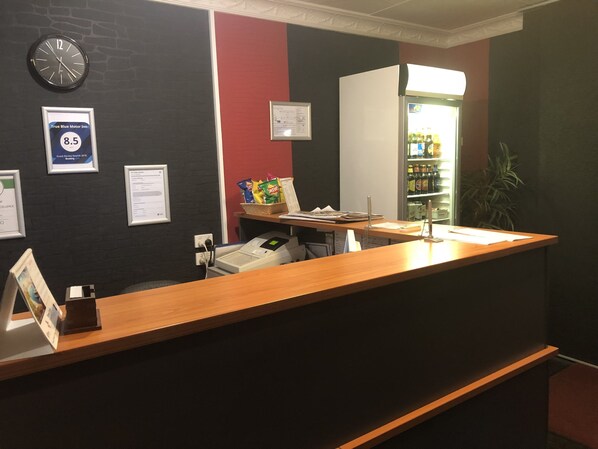 A reception desk with a clock, framed awards, and a refrigerator stocked with beverages.