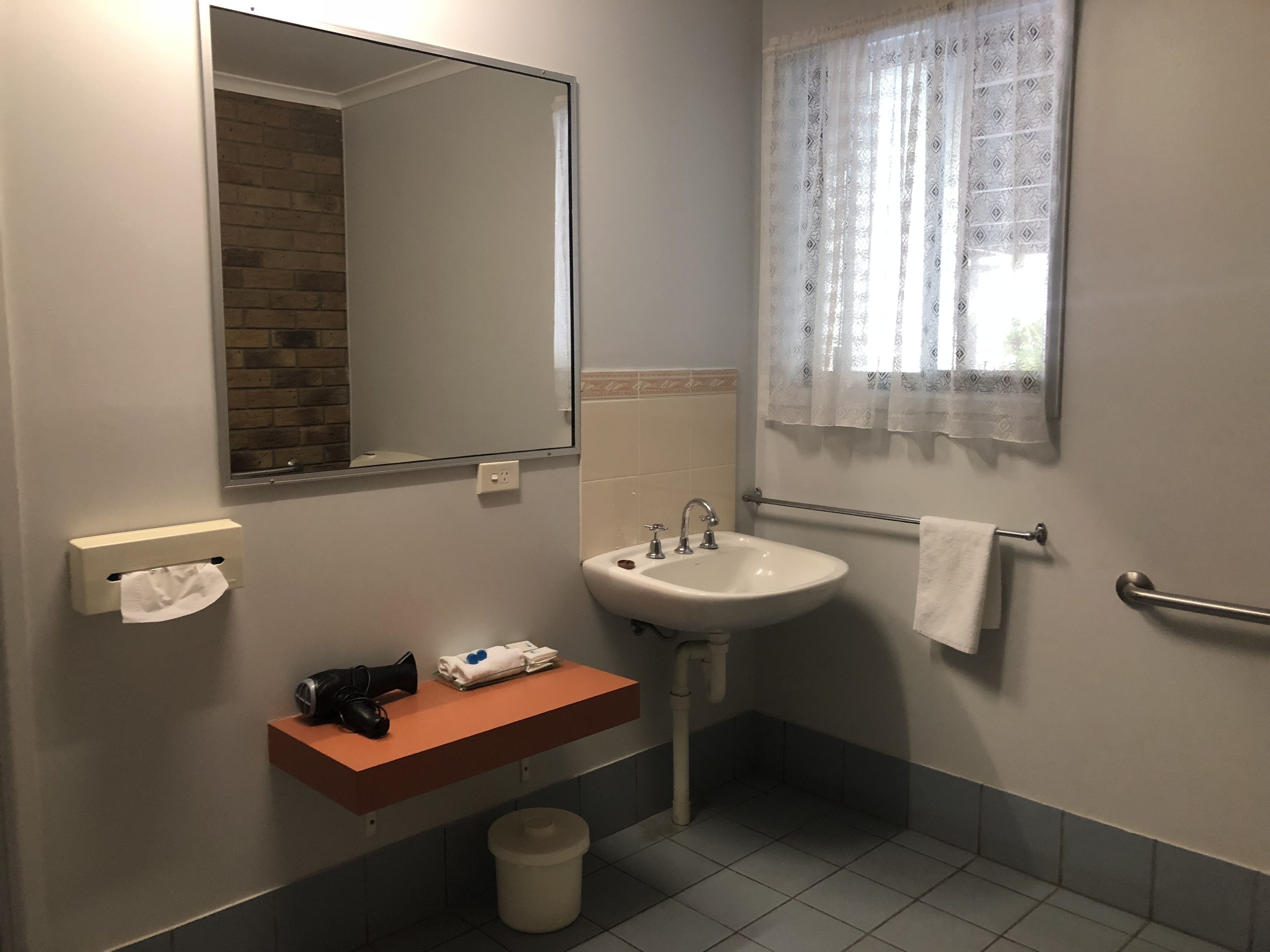 A bathroom with a sink, mirror, towel rack, and a window with patterned curtains.