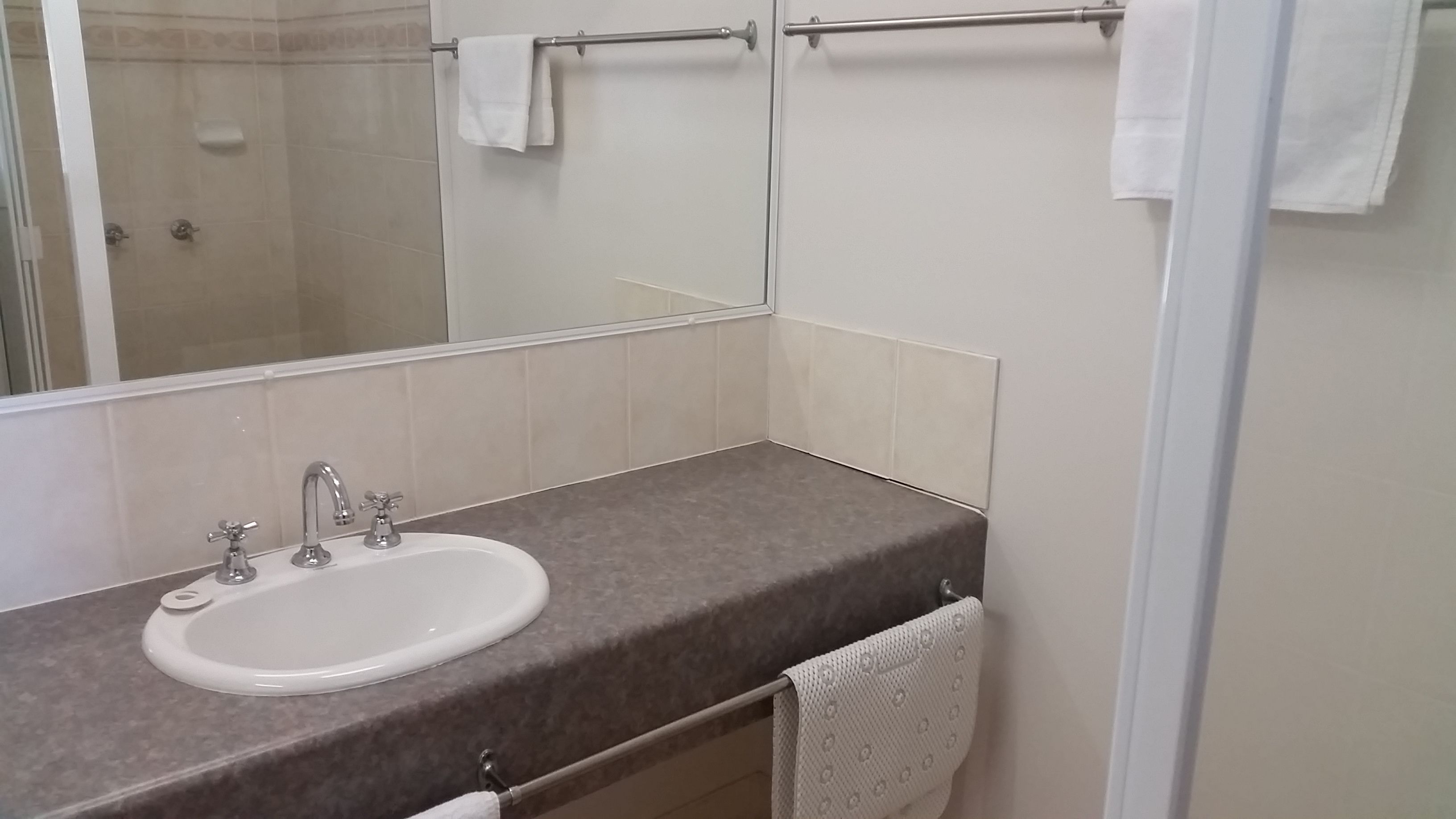 A bathroom with a white sink, two faucets, a towel rack, and a mirror.
