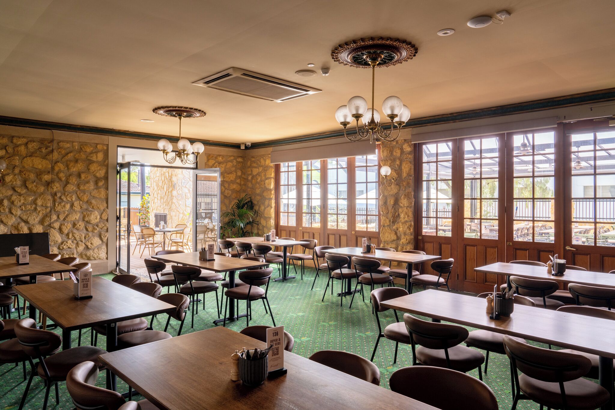 A restaurant with stone walls, large windows, and multiple tables and chairs.