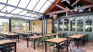 Un patio al aire libre con mesas y sillas de madera, paredes de piedra y techo de vidrio.