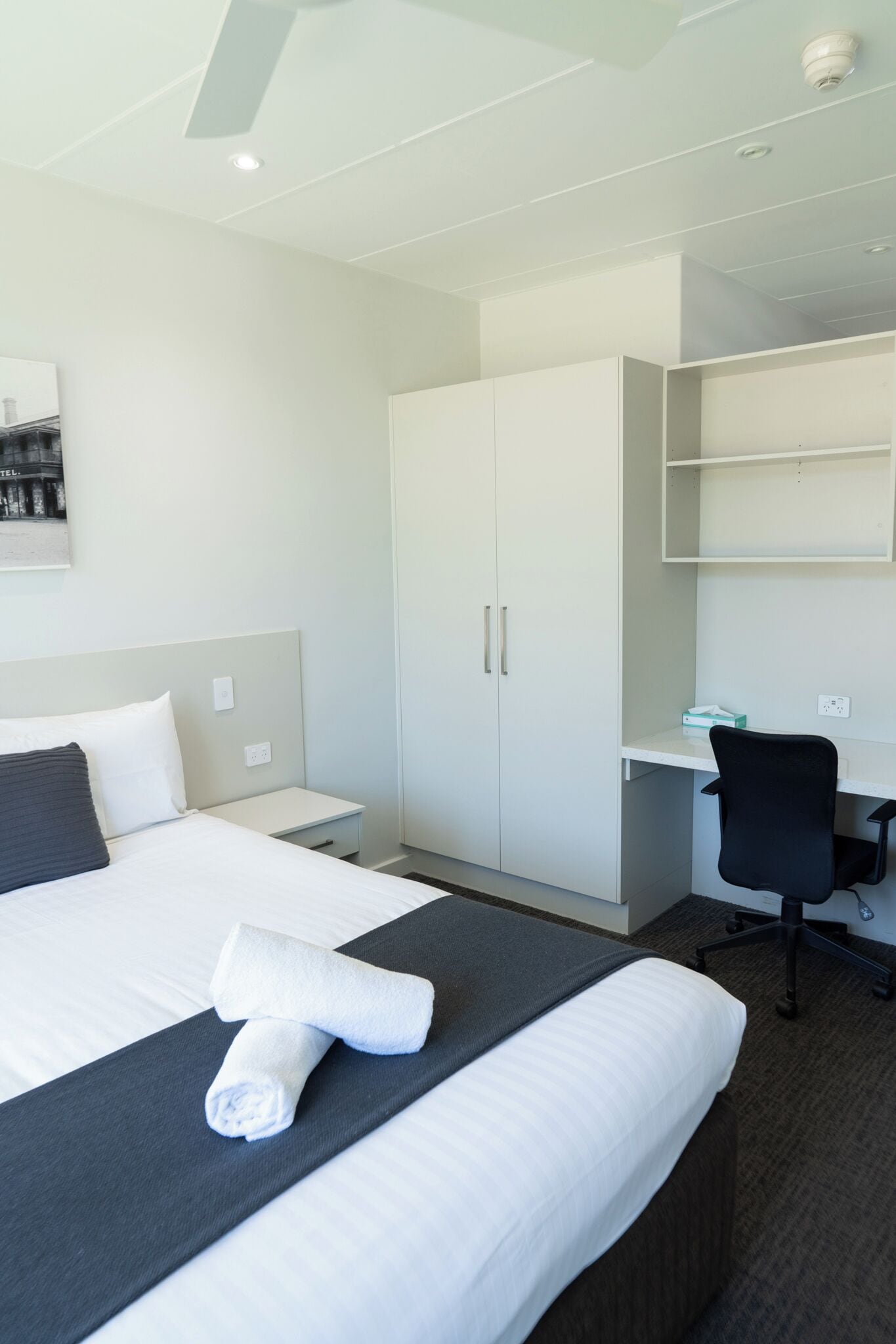 A hotel room with a neatly made bed, a desk, and a wardrobe.