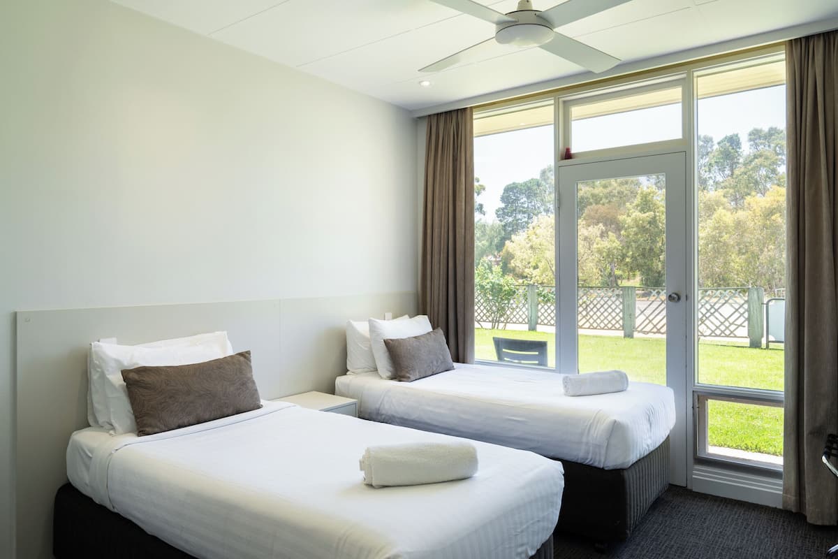 A hotel room with two beds, a ceiling fan, and a large window with curtains.
