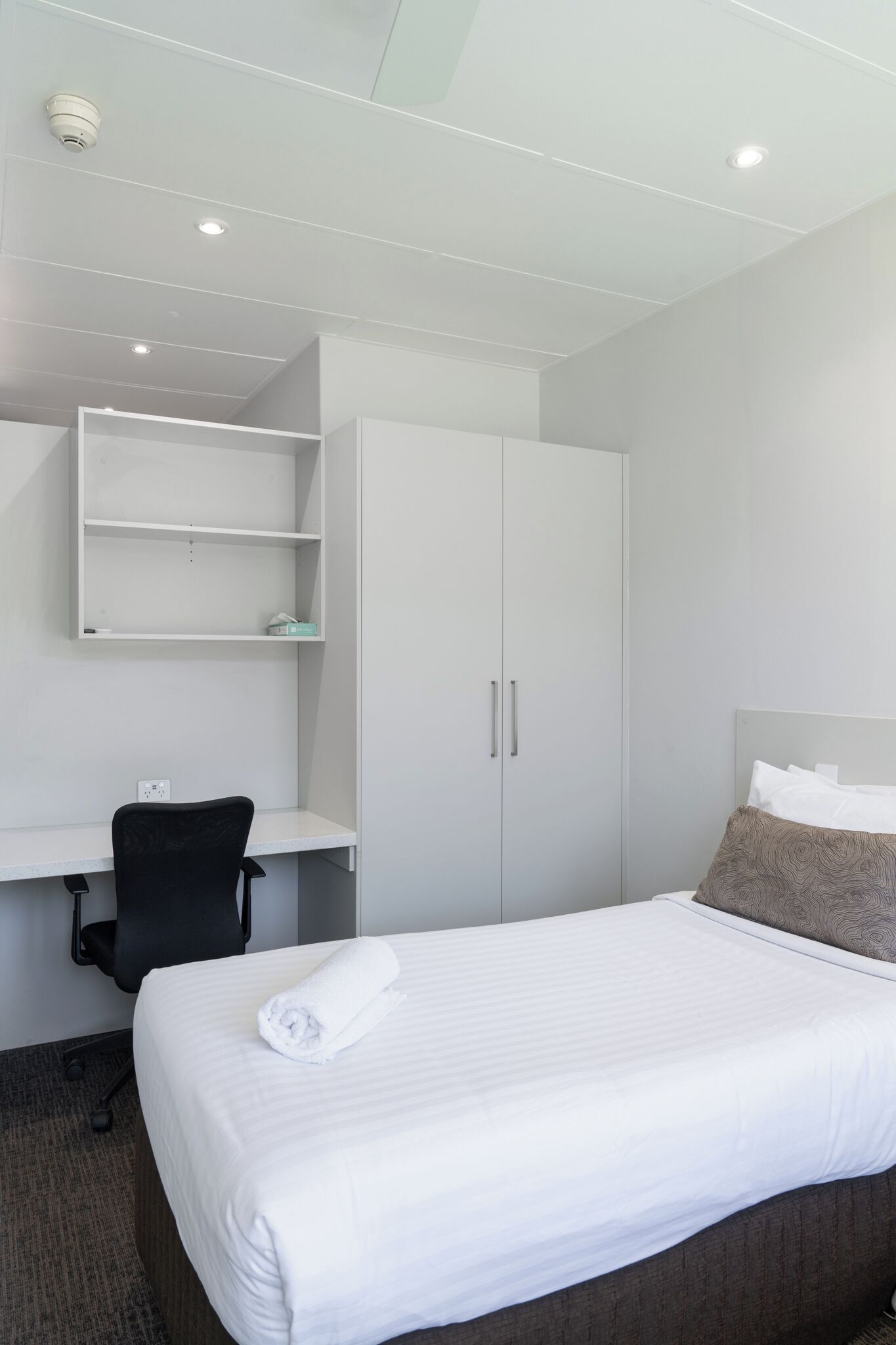A hotel room with a neatly made bed, a desk with a chair, and a wardrobe.