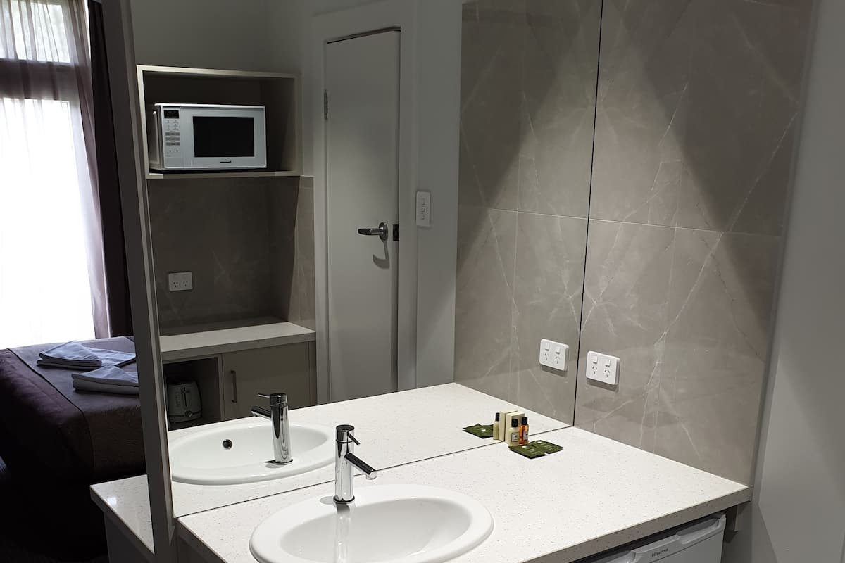 A modern bathroom with a double sink, a mirror, a microwave, and a small cabinet.