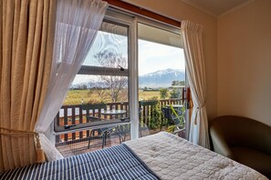 A bedroom with a bed, a chair, and a balcony with a view of mountains. - Brook House Bed & Breakfast and Cottages (Kaikōura)
