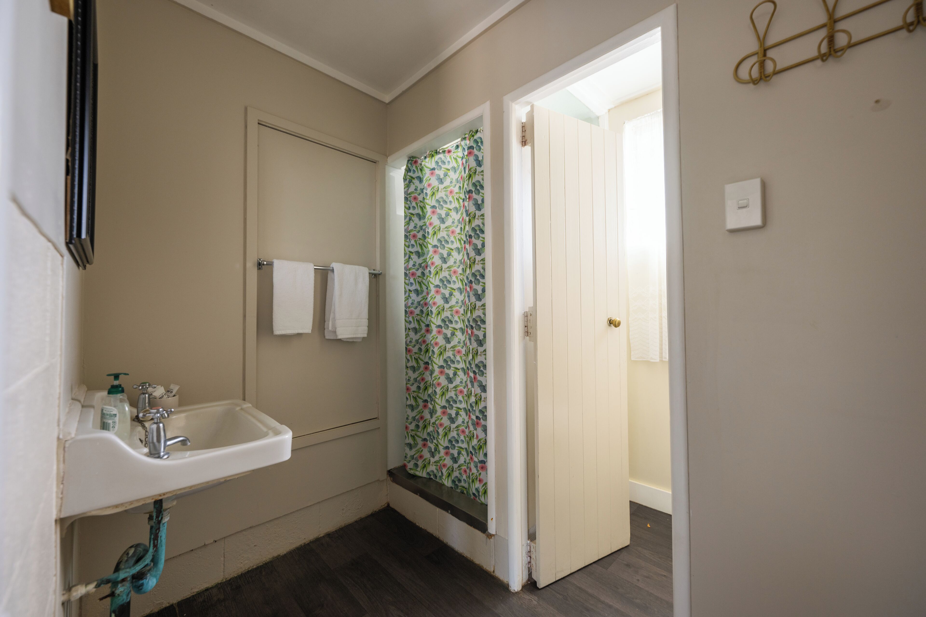 A bathroom with a sink, a shower with floral curtains, and a door leading to another room.