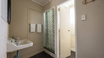 A bathroom with a sink, a shower with floral curtains, and a door leading to another room.