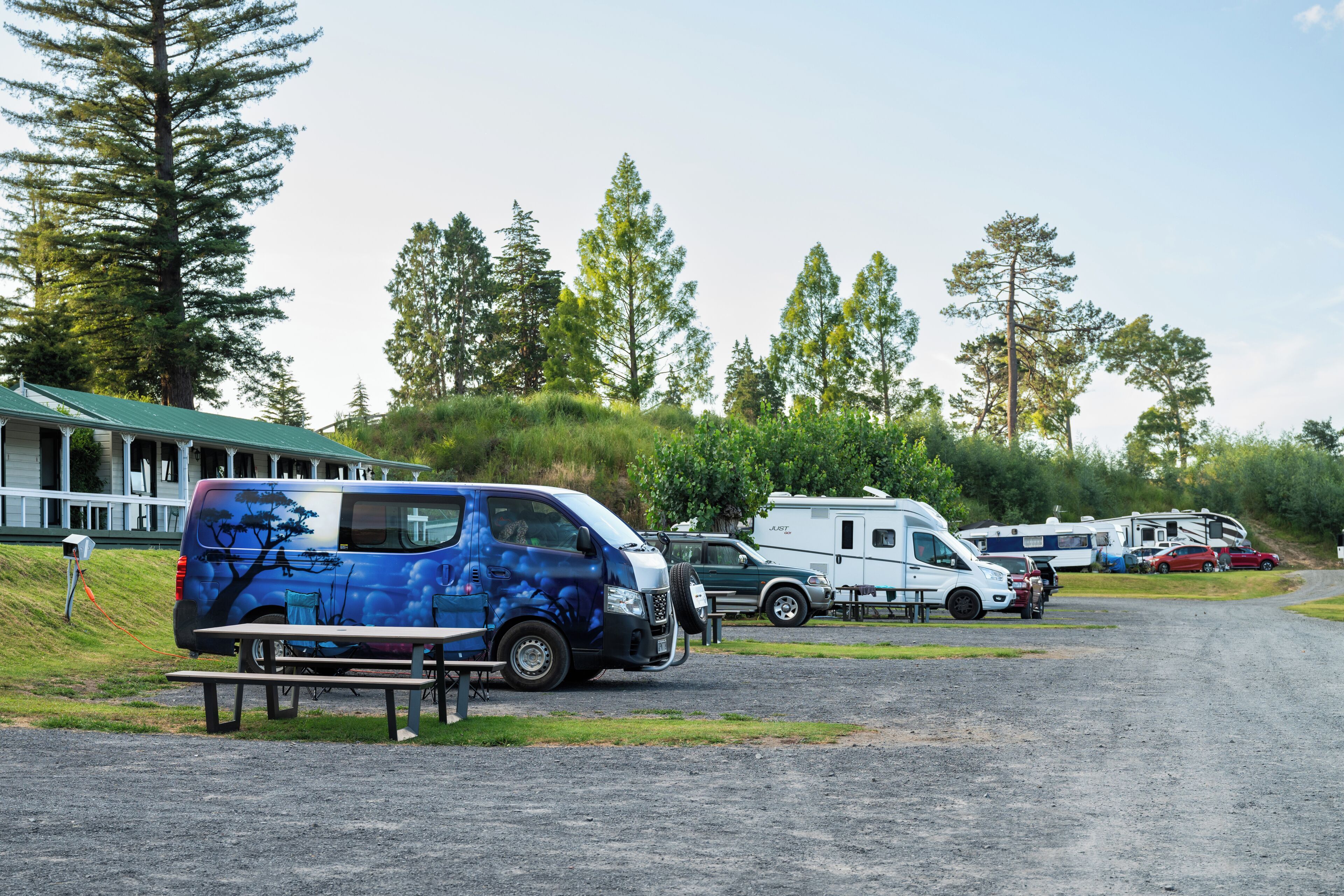 A campground with RVs and a blue van parked near picnic tables.