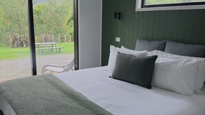 Une chambre avec un grand lit, un mur vert et une fenêtre donnant sur un jardin.