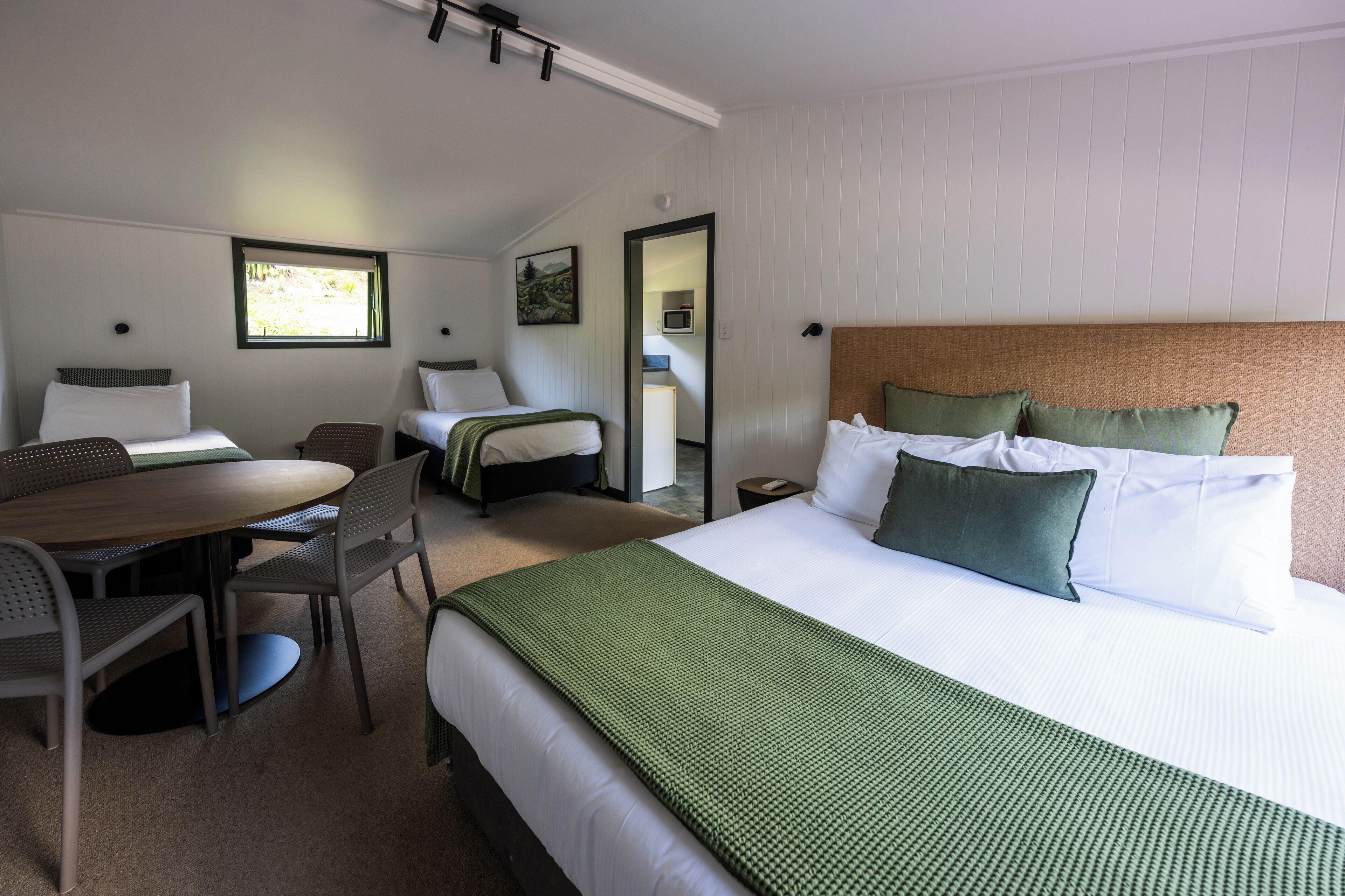 Une chambre d’hôtel avec un grand lit, une table à manger avec des chaises, une petite kitchenette et une salle de bain visible à travers une porte ouverte.