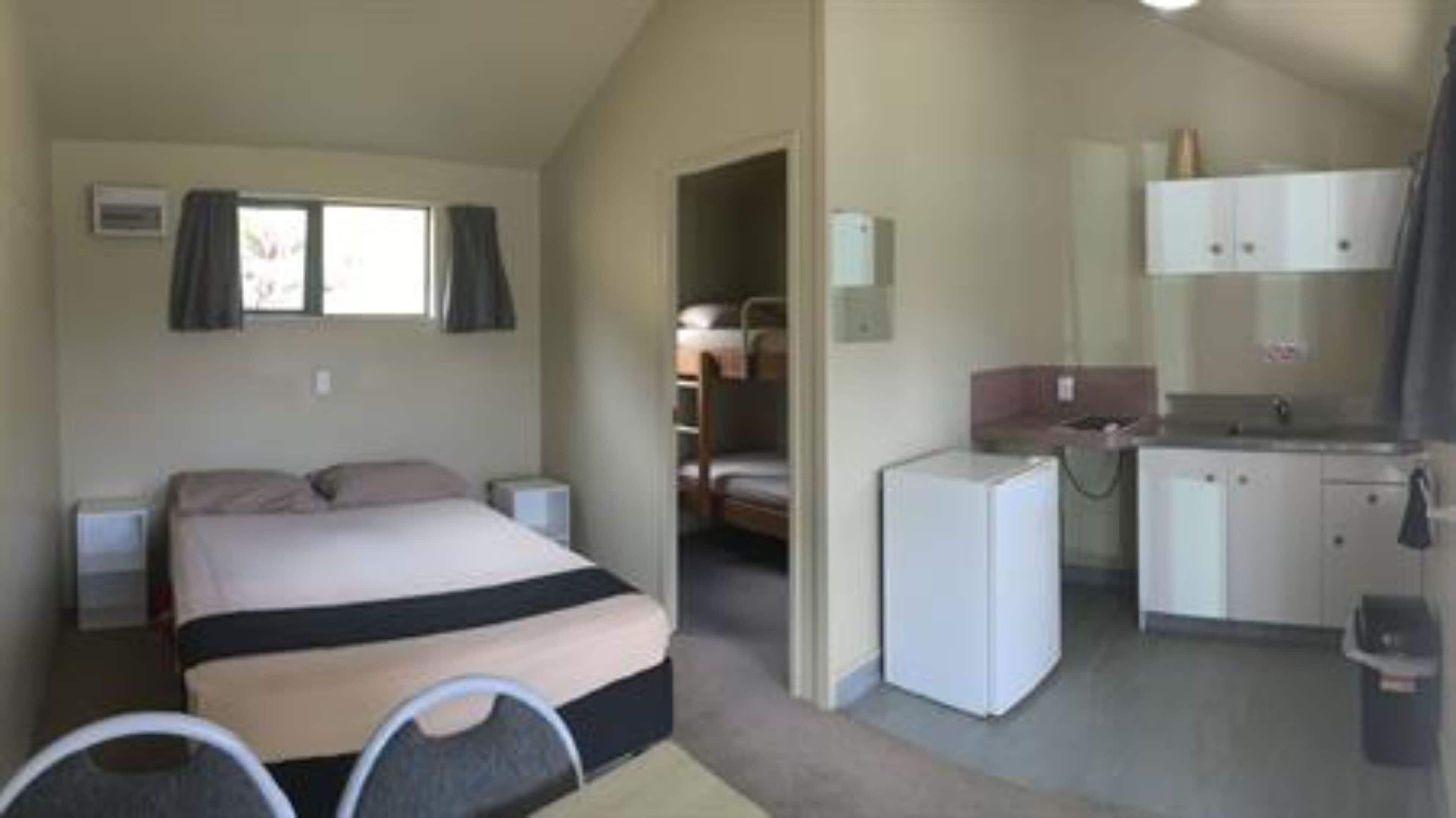 A compact room with a bed, a small kitchenette, and a bathroom.