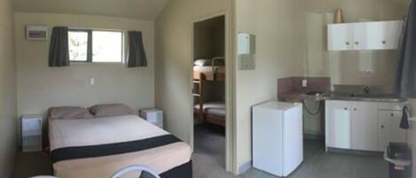 A compact room with a bed, a small kitchenette, and a bathroom.