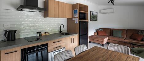 A modern kitchen with wooden cabinets, a built-in microwave, and a black refrigerator. There is a dining area with a wooden table and chairs.