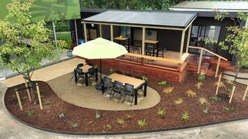 Un espace extérieur aménagé en terrasse, avec des tables et des chaises, entouré d’un jardin paysager agrémenté de paillis et de petites plantes.