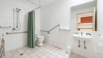 A bathroom with a shower, toilet, grab bars, and a sink.