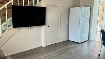 Una sala de estar con un televisor de pantalla plana montado en la pared, una puerta blanca y un refrigerador blanco.