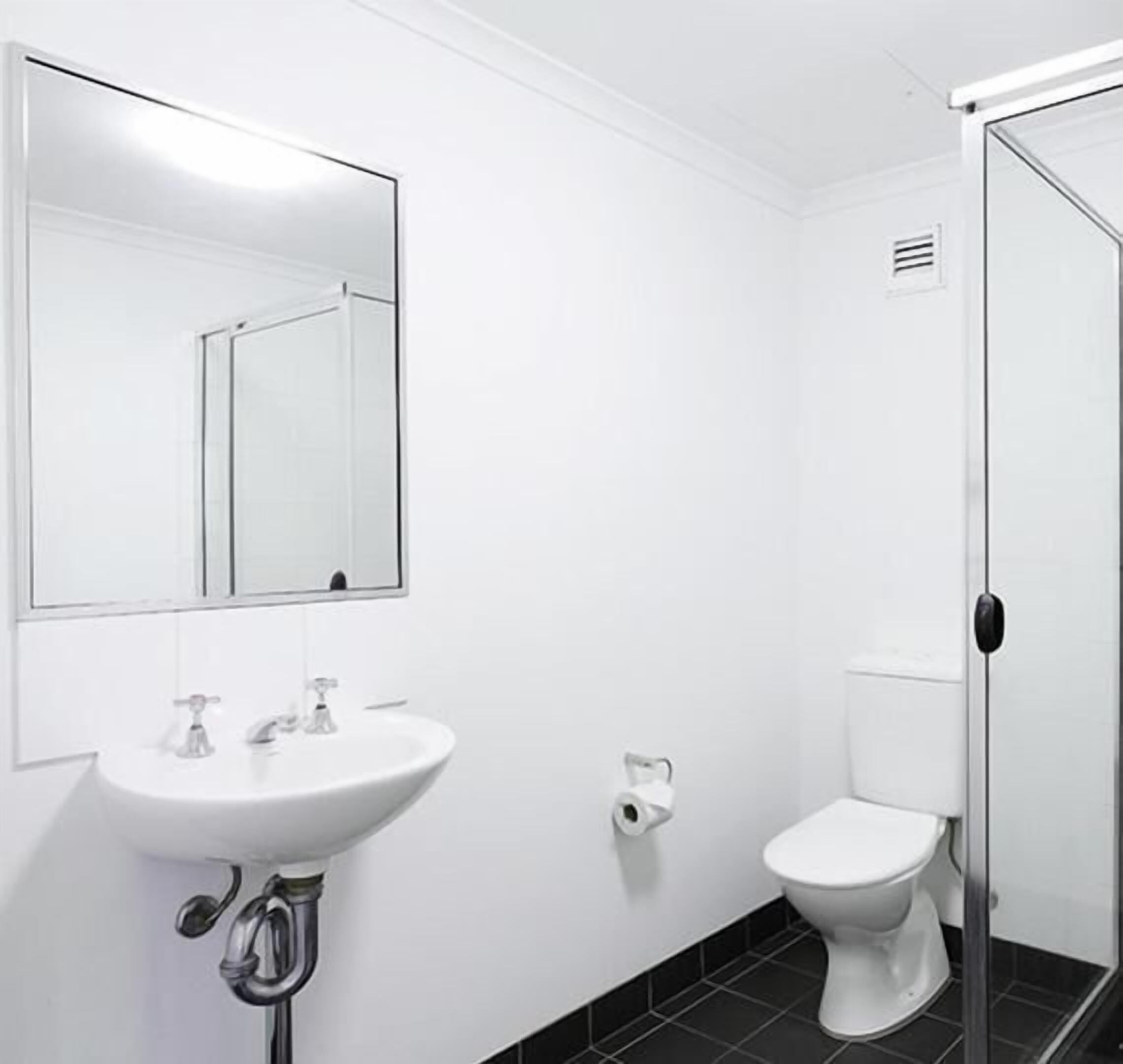 A bathroom with a white sink, a mirror, a toilet, and a shower door.