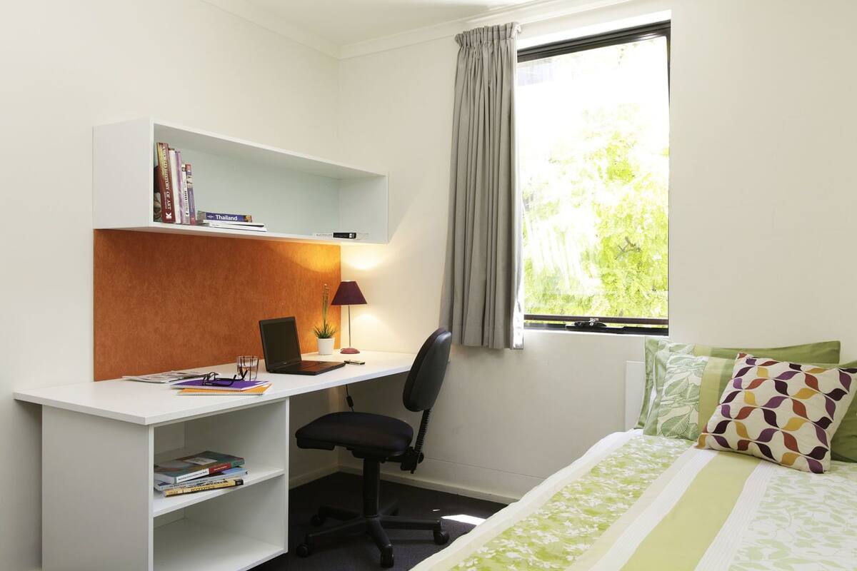 Quarto de hotel com escrivaninha, cadeira e cama com roupa de cama estampada.
