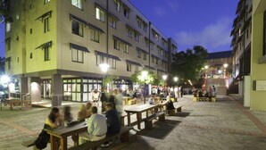 An outdoor seating area with tables and benches, surrounded by buildings with multiple floors and windows. - Sydney University Village (Newtown)