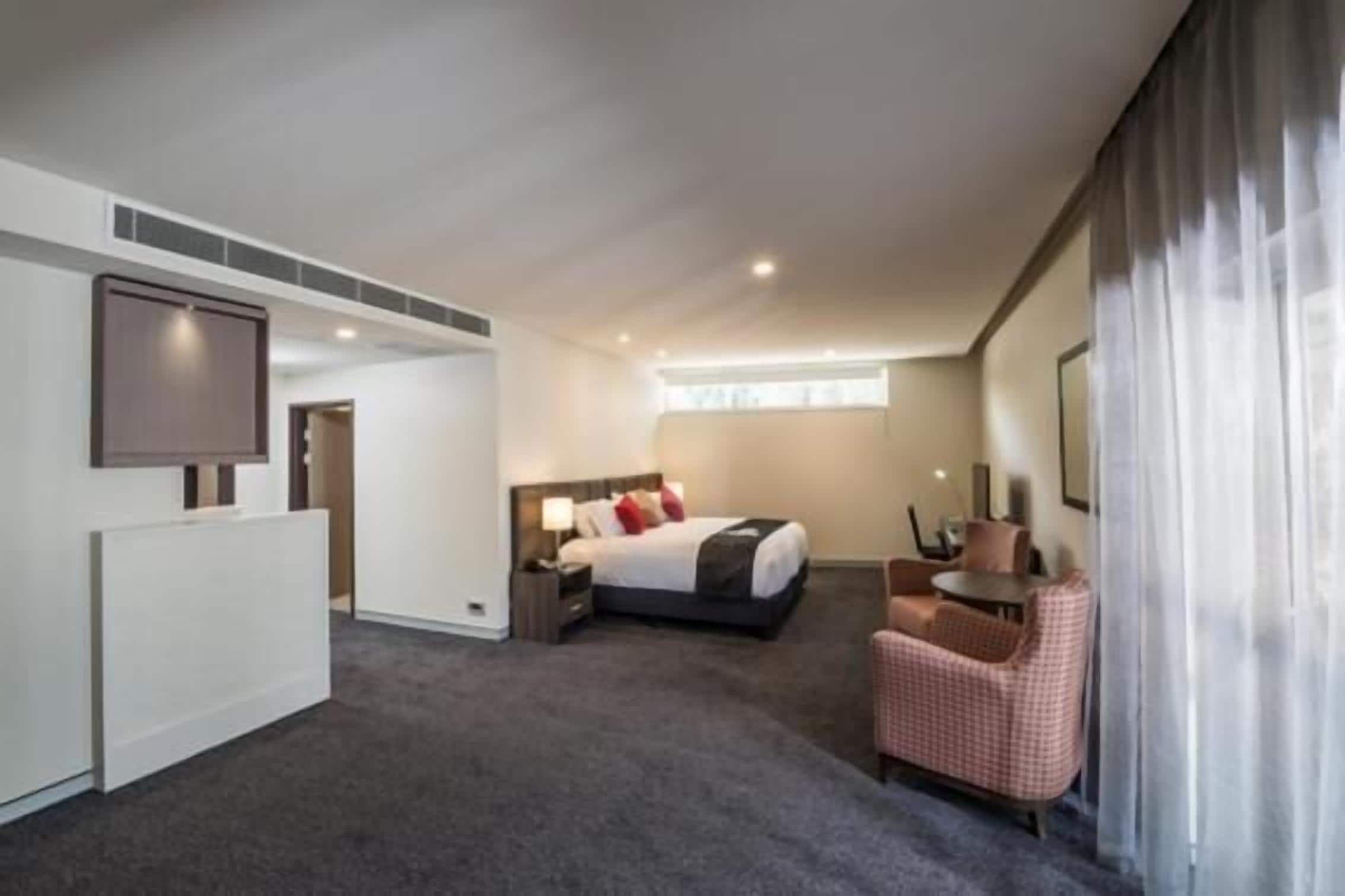 A hotel room with a bed, a chair, a desk, and a large window.