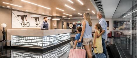 A modern reception desk with a digital display, a wooden ceiling, and a glass wall reflecting the interior.