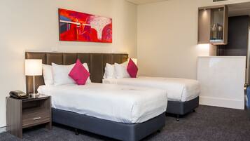 A hotel room with two beds, a nightstand with a lamp, a painting on the wall, and a refrigerator.