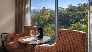A room with a large window, two patterned chairs, a small round table, and two glasses of white wine.