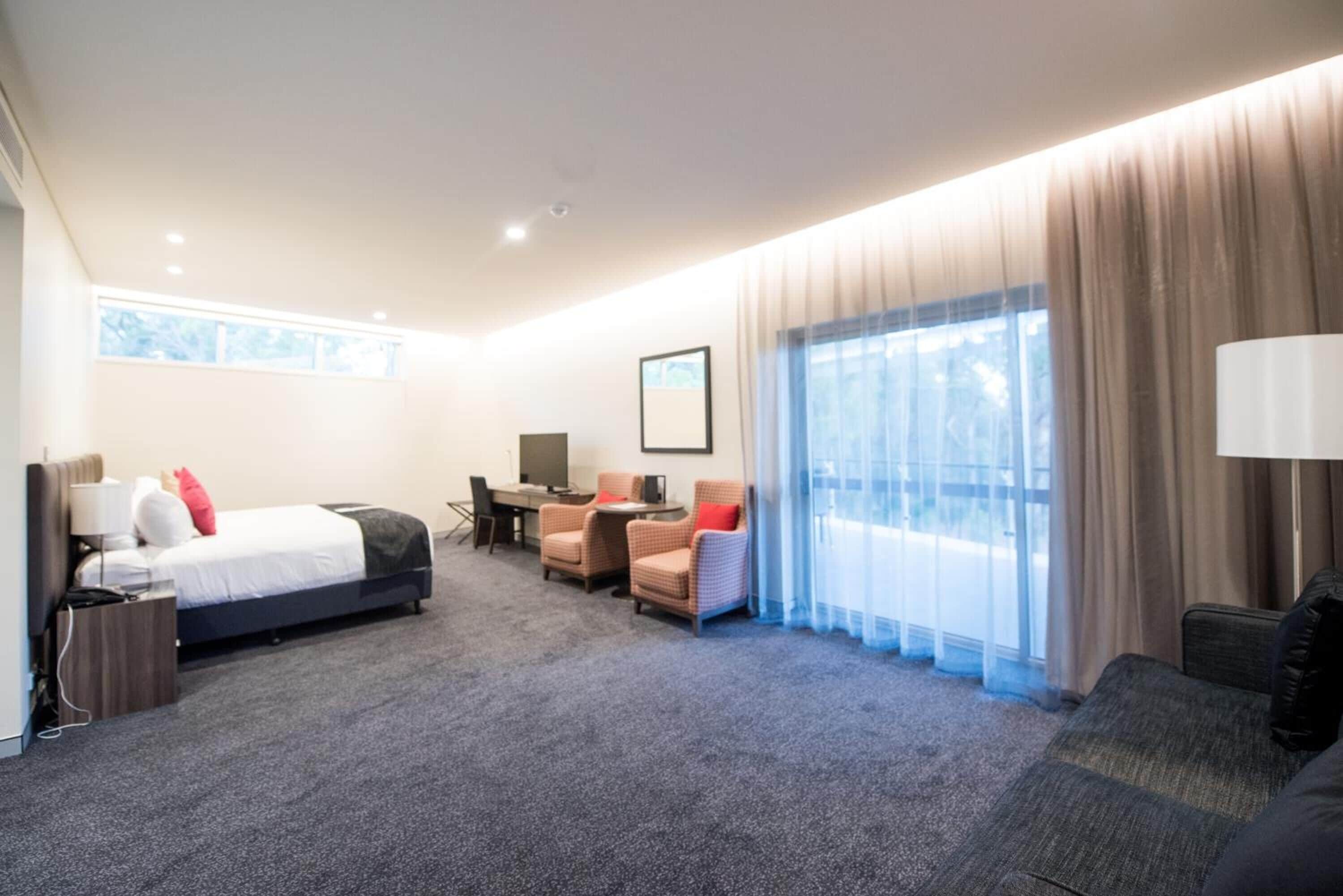 Una habitación de hotel con cama, escritorio, dos sillas, sofá, televisor y un ventanal con cortinas.