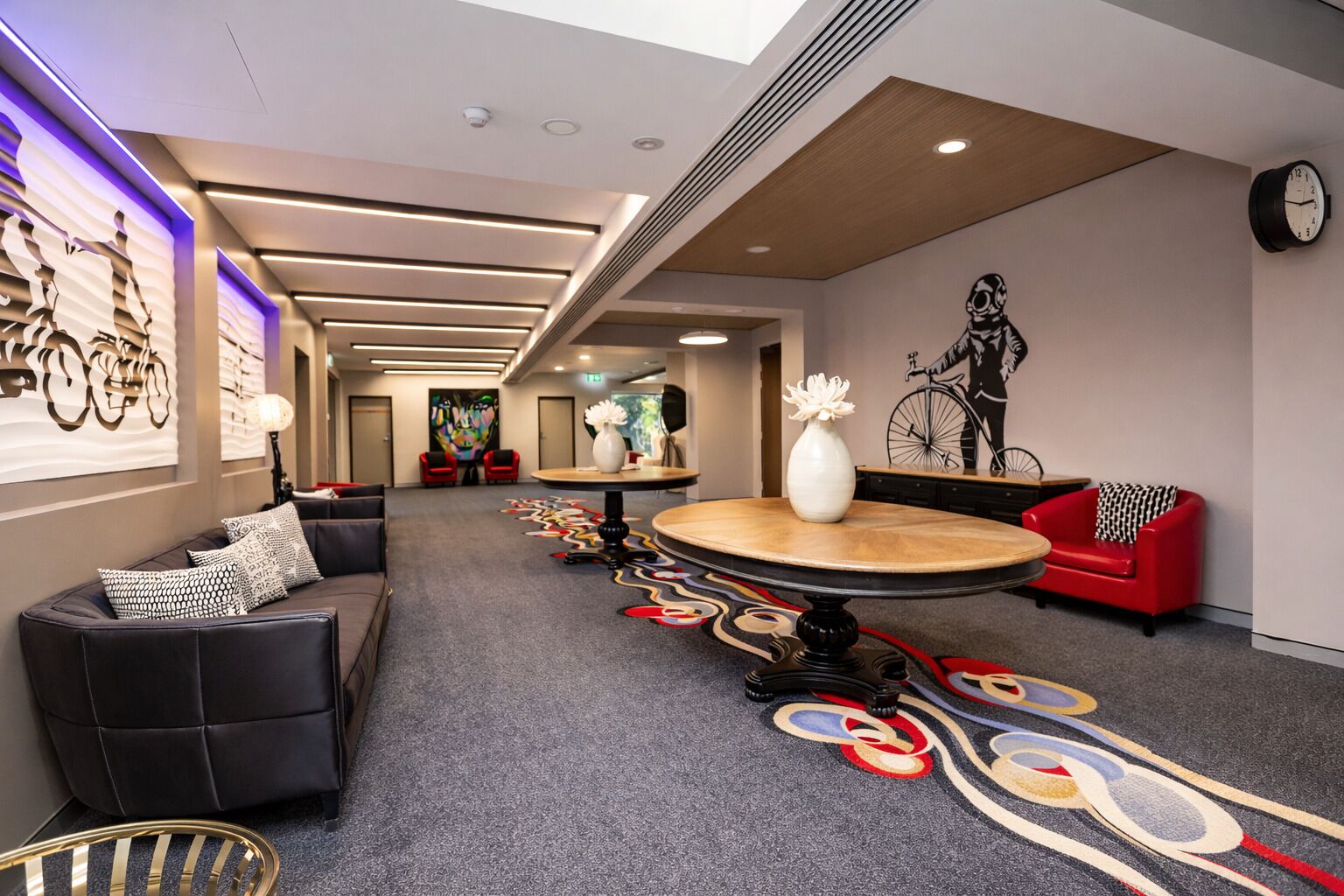 A hotel lobby with a round table, sofas, a patterned carpet, and artwork on the walls.