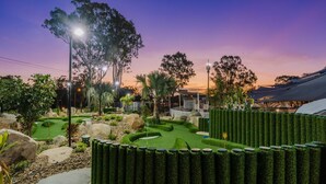 A well-maintained golf course with neatly trimmed hedges, a putting green, and a variety of trees and shrubs.