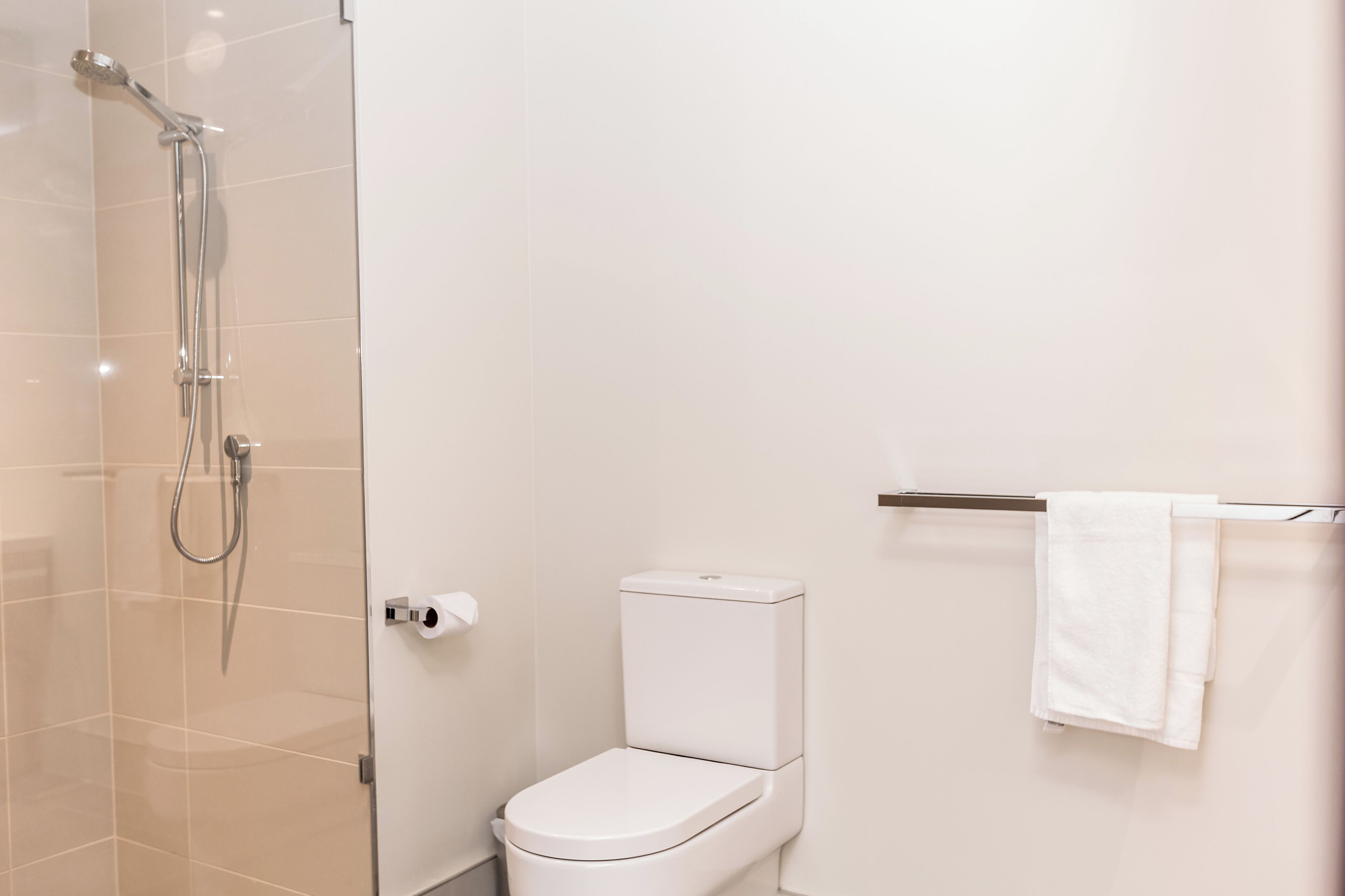 A modern bathroom with a glass shower enclosure, a white toilet, and a towel rack with a white towel.
