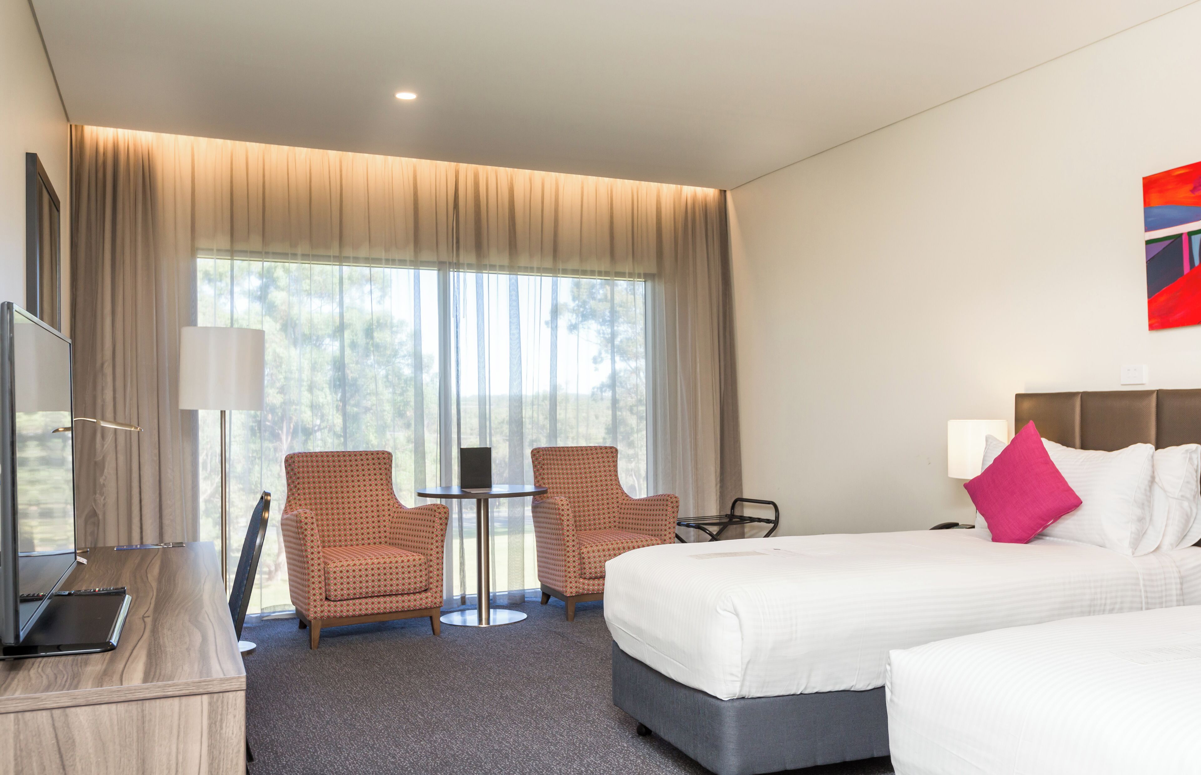 Ein Hotelzimmer mit einem Bett, zwei Sesseln, einem Schreibtisch und einem Laptop.