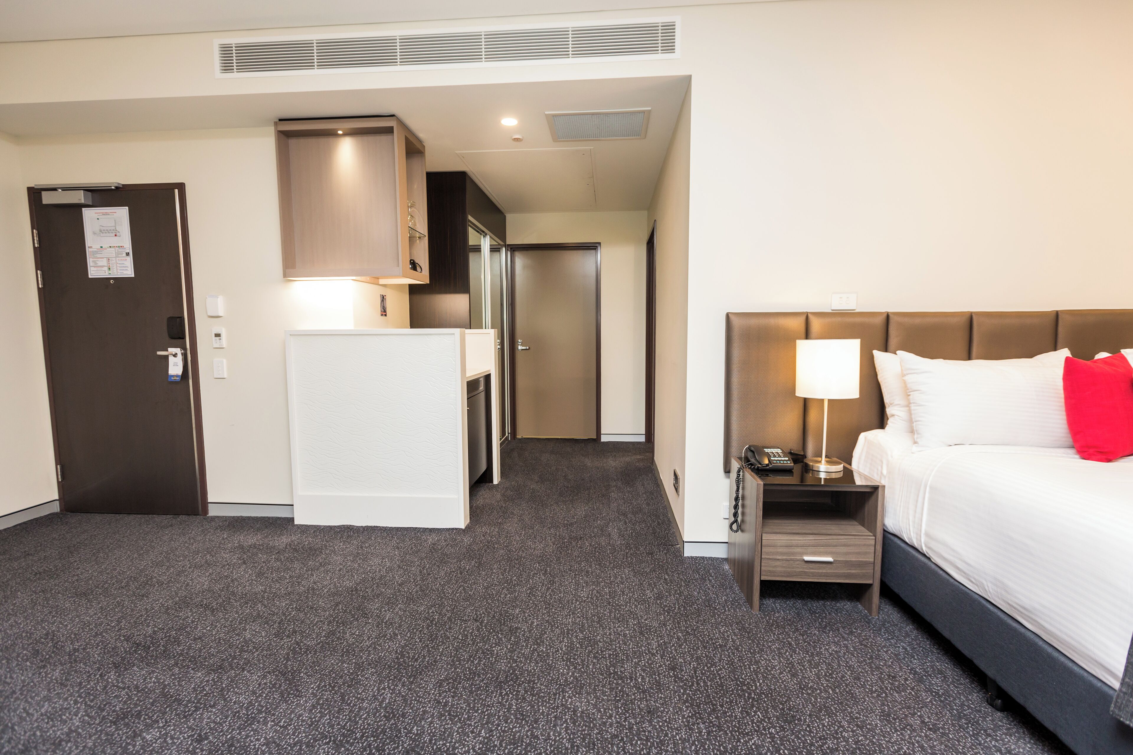 Une chambre d’hôtel comprenant un lit, une table de chevet, un bureau, une kitchenette et une porte.