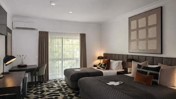 Une chambre d’hôtel avec un lit, un bureau, une chaise, une lampe et une grande fenêtre avec des rideaux.
