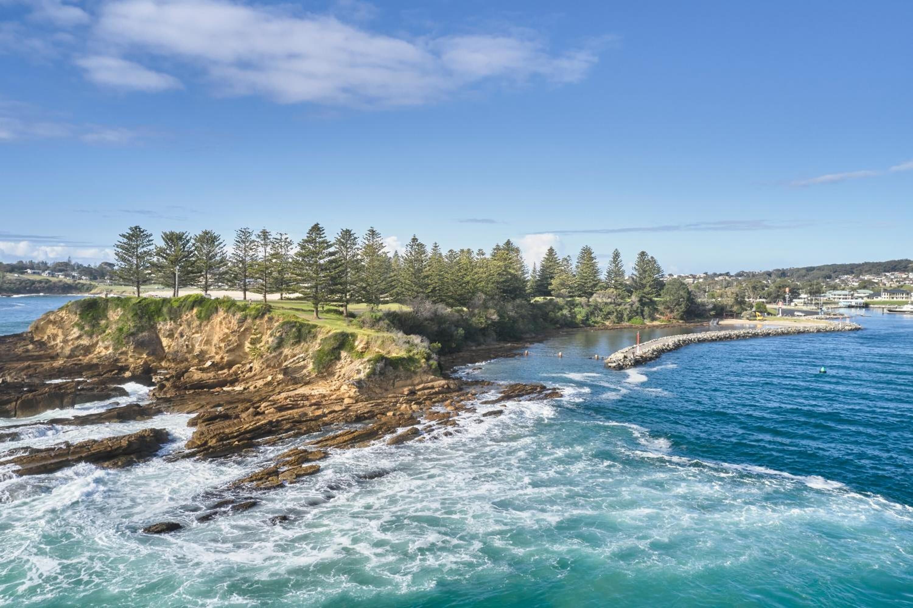 A coastal landscape with rocky cliffs, a beach, and a clear blue sky.